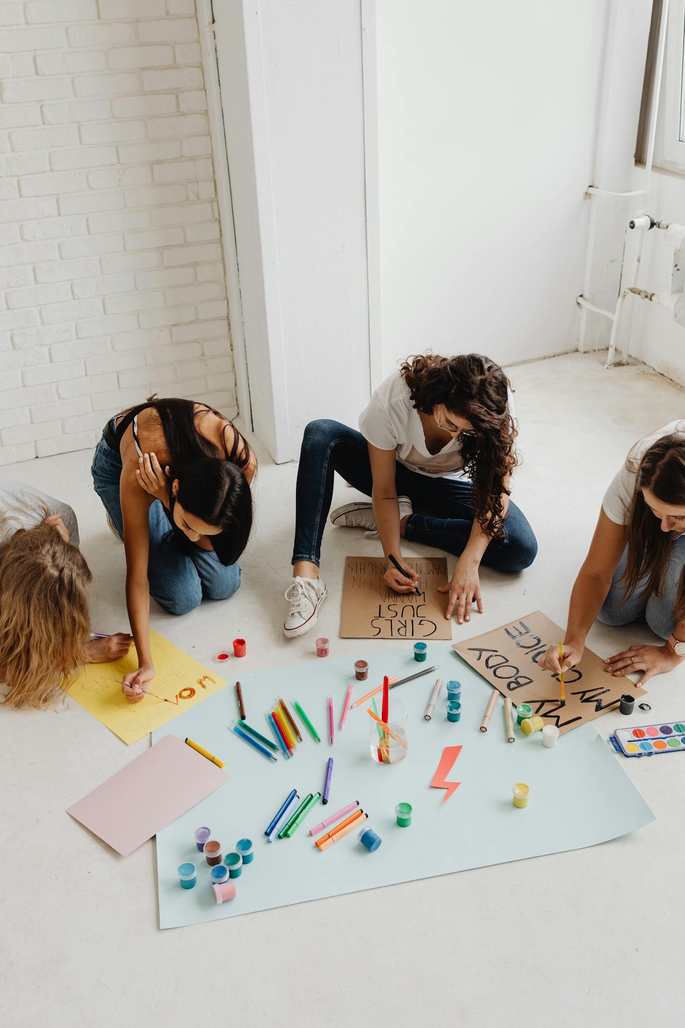 A diverse group of women sitting indoors, creating activist posters with art supplies, promoting creativity and unity.