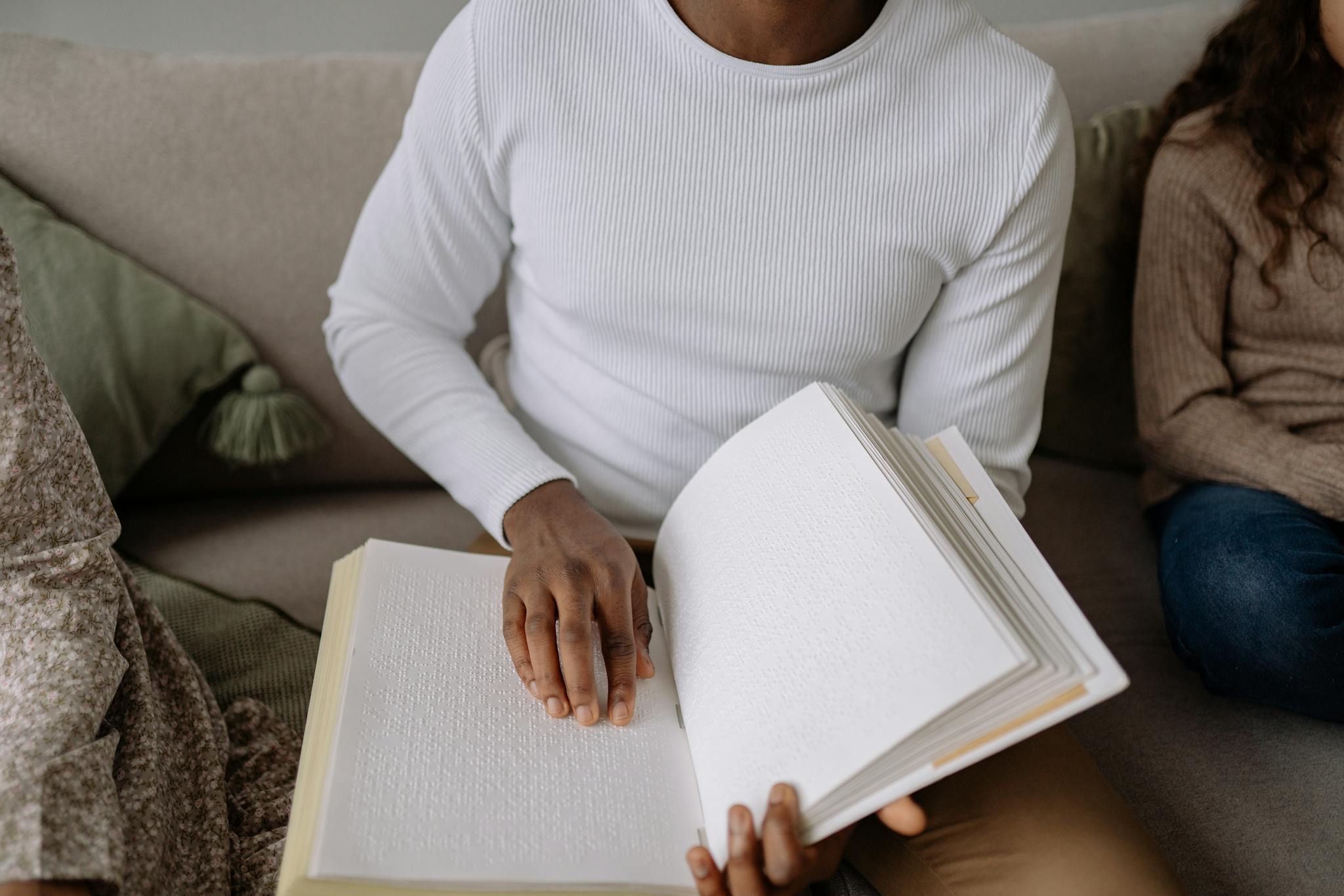 Close-up of hands reading a Braille book indoors, emphasizing tactile learning.