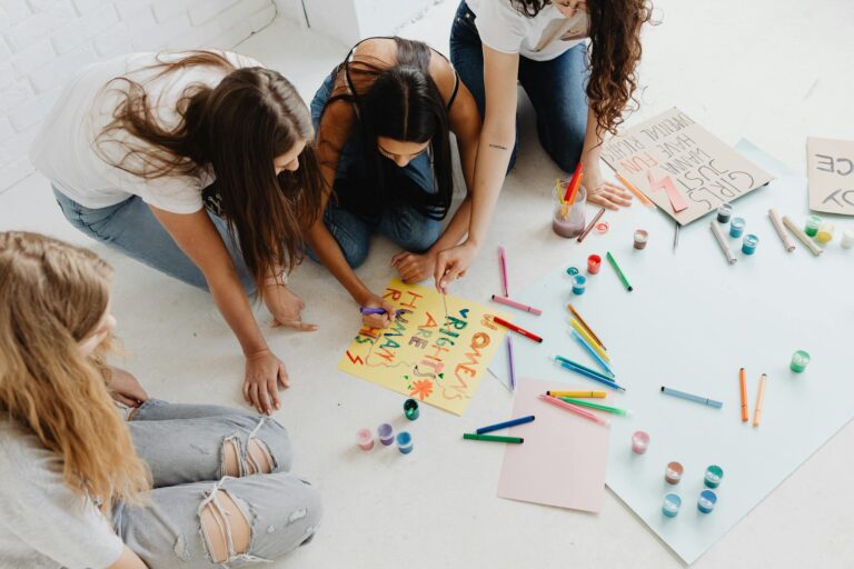 Group of women designing artistic placards with colorful materials.