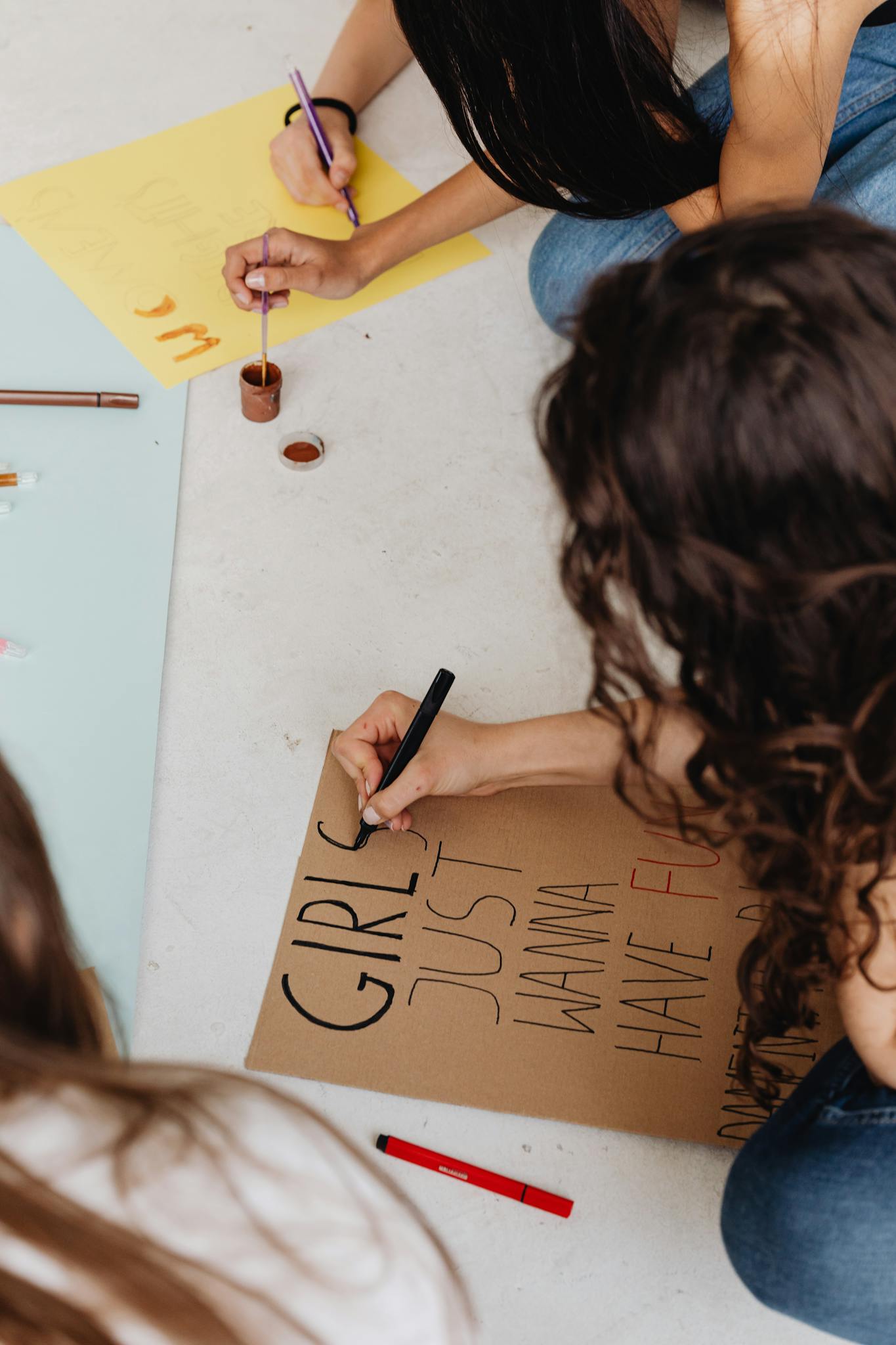 Three women sitting and painting message posters for empowerment.