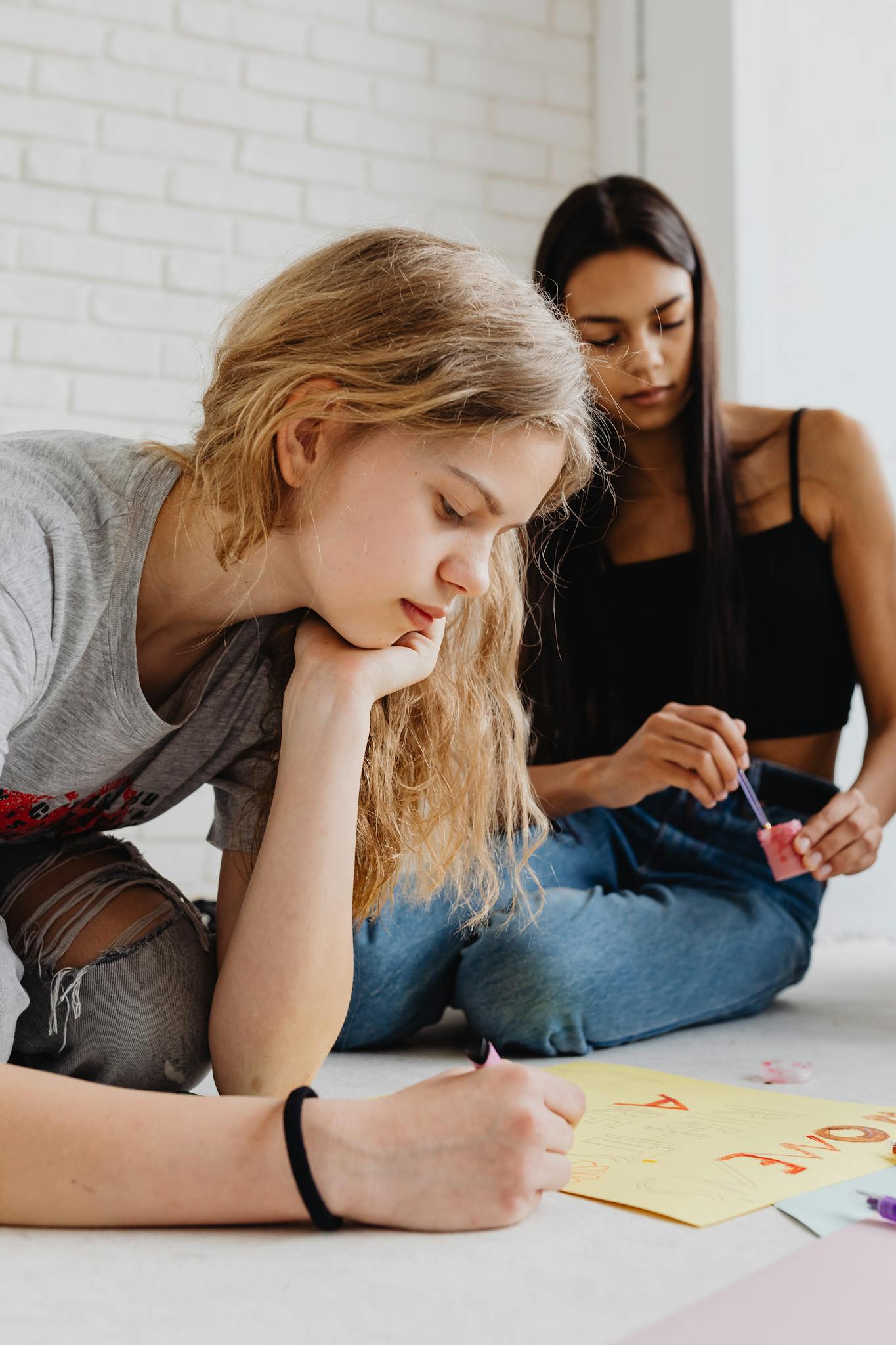 Two women creating art with paper and pencils on the floor indoors.