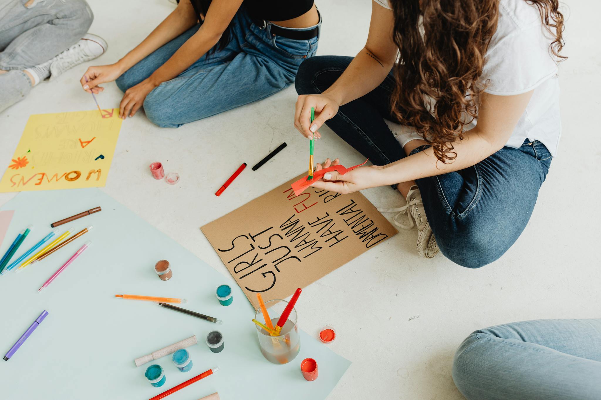Women creating protest signs with paints and brushes, symbolizing activism and creative expression.